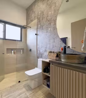 Bano privado moderno con ducha en vidrio, sanitario y lavamanos de diseno.
