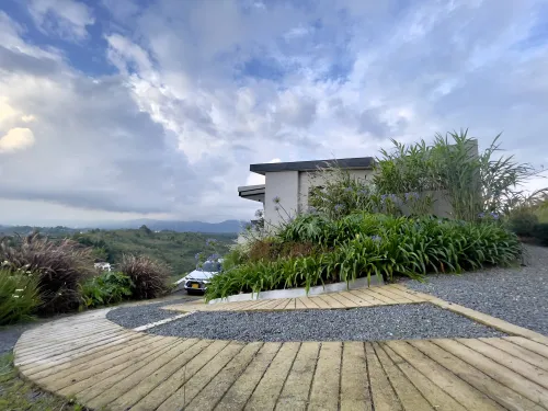 Acceso exterior de casa campestre con jardines decorativos y vista natural al paisaje.