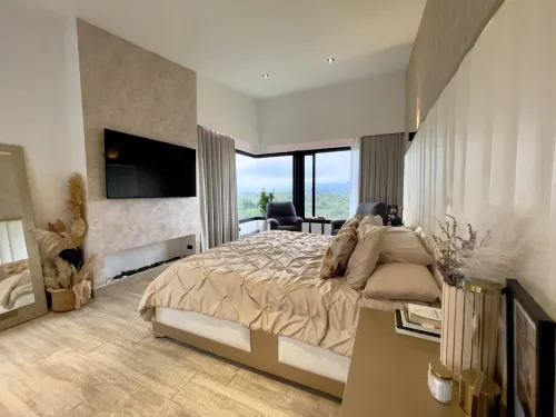 Alcoba principal con chimenea, televisor y gran ventanal con vista natural.