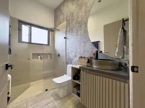 Bano privado moderno con ducha en vidrio, sanitario y lavamanos de diseno.