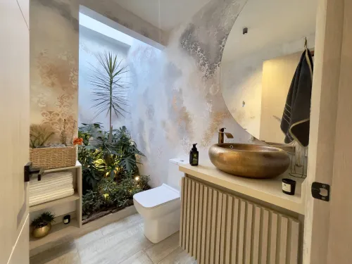 Bano social con jardin interior, espejo redondo y lavamanos decorativo.