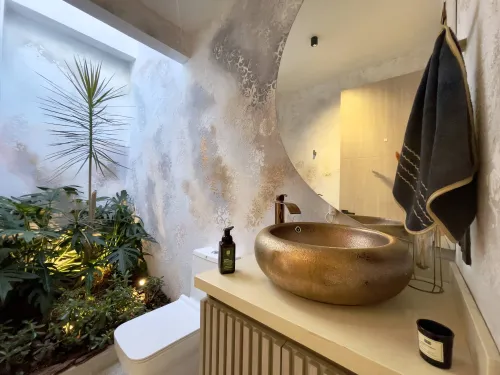 Bano social de diseno con lavamanos dorado y muro decorativo elegante.