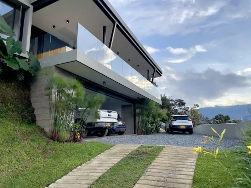 Entrada principal de casa campestre moderna con acceso vehicular, garaje y fachada contemporanea.